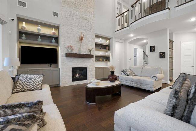 This spacious living room features high ceilings, a cozy fireplace, and elegant built-in shelves. The open design includes a modern color palette with neutral tones, hardwood floors, and a stylish staircase leading to an upper level. Ideal for comfortable living and entertaining. | Image 24