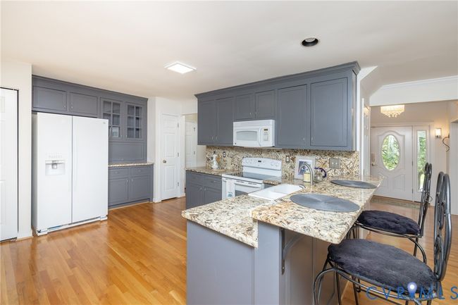 Kitchen with white appliances, a peninsula, decorative backsplash, light wood-type flooring, and ornamental molding | Image 12