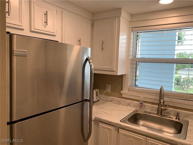 Kitchen featuring stainless steel fridge, sink, and white cabinetry | Image 11