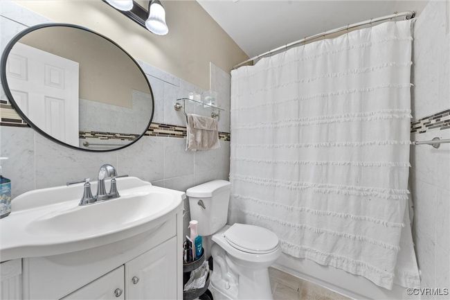 Bathroom featuring tile walls, shower / bathtub combination with curtain, toilet, and vanity | Image 19