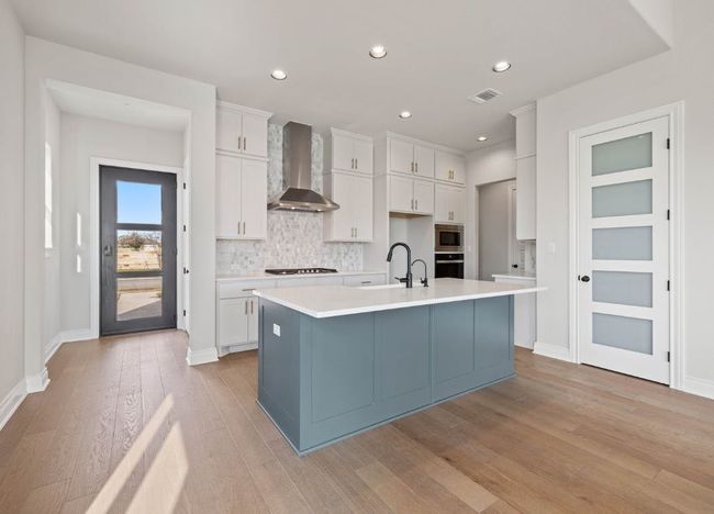 Kitchen featuring light wood finished floors, a sink, stainless steel appliances, tasteful backsplash, and wall chimney range hood | Image 11
