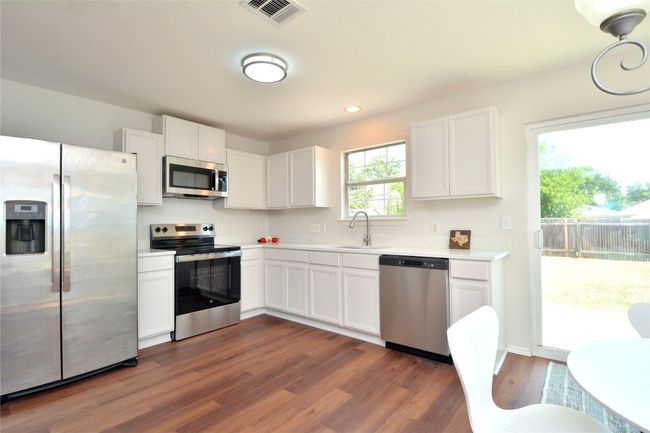 Kitchen featuring stainless steel appliances, a sink, light countertops, dark wood-type flooring, and white cabinets | Image 4