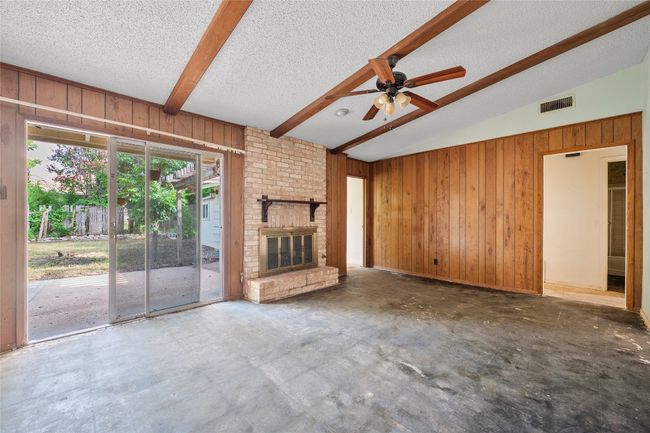 Unfurnished living room featuring wooden walls, a textured ceiling, a ceiling fan, a brick fireplace, and concrete floors | Image 12