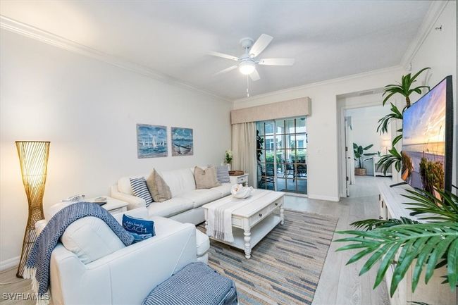 Living room with crown molding, ceiling fan, and light wood-style flooring enjoys direct access to the screened lanai | Image 6