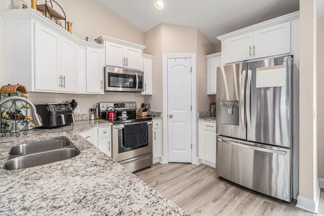 Kitchen featuring appliances with stainless steel finishes, lofted ceiling, white cabinets, light wood-style flooring, and recessed lighting | Image 7