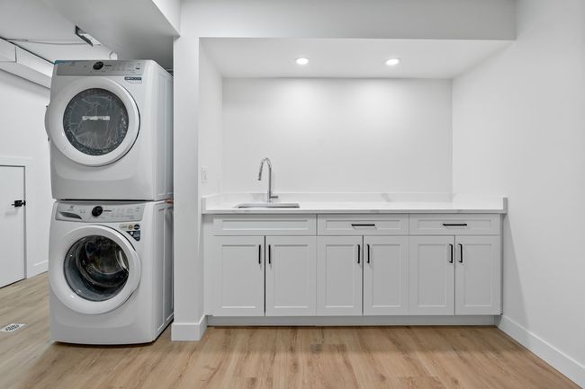 Laundry room with stacked washer / dryer, light wood-style flooring, baseboards, and a sink | Image 18