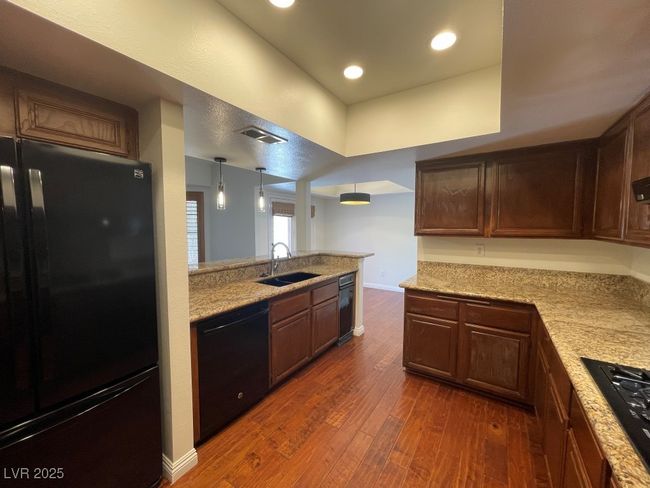 Kitchen featuring black appliances, dark wood-type flooring, recessed lighting, a peninsula, and light stone counters | Image 7