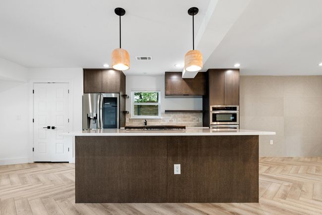 Kitchen featuring hanging light fixtures, dark brown cabinetry, light countertops, appliances with stainless steel finishes, and visible vents | Image 14