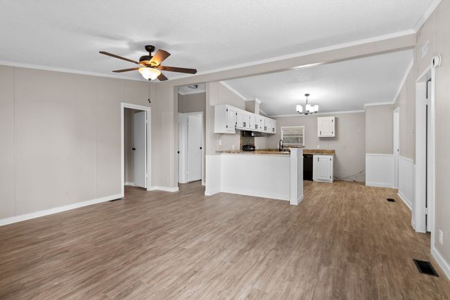 Unfurnished living room with a chandelier, light wood-style flooring, a ceiling fan, and crown molding | Image 13