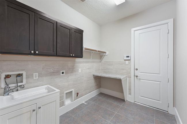 This laundry room is super practical—tiled floors for easy cleanup, a utility sink, and plenty of cabinets and counter space for sorting and folding. You’ve got hookups for gas and electric dryers, plus a door that makes dropping off muddy shoes or hauling in groceries a breeze. | Image 19