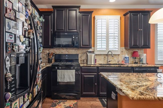 Kitchen with black appliances, a sink, light stone countertops, healthy amount of natural light, and crown molding | Image 4