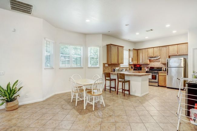 Kitchen featuring appliances with stainless steel finishes, under cabinet range hood, tasteful backsplash, a peninsula, and light tile patterned flooring | Image 5
