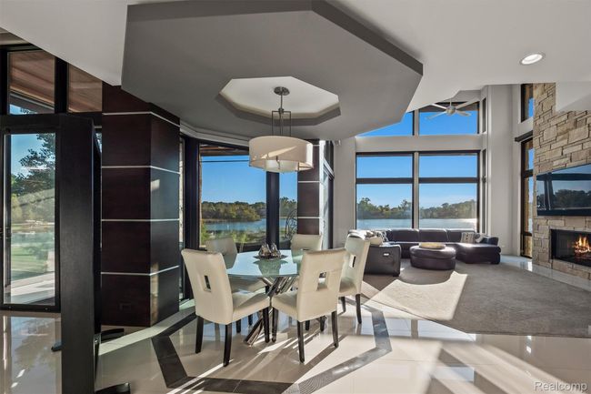 Tiled dining room featuring a water view, a stone fireplace, ceiling fan, and a tray ceiling | Image 11