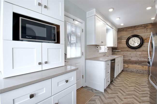Kitchen featuring a sink, wood walls, dishwasher, white cabinetry, and light countertops | Image 10