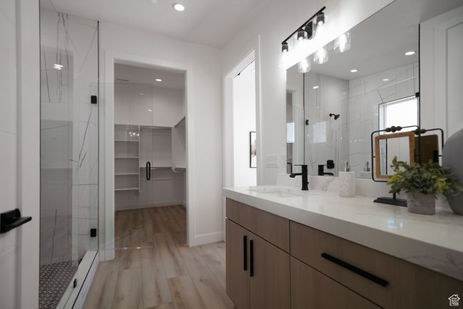 Full bath featuring a shower stall, double vanity, wood finished floors, a walk in closet, and recessed lighting | Image 10