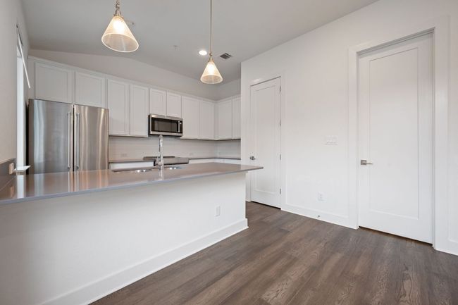 Kitchen featuring stainless steel appliances, dark wood-type flooring, white cabinets, decorative backsplash, and decorative light fixtures | Image 6