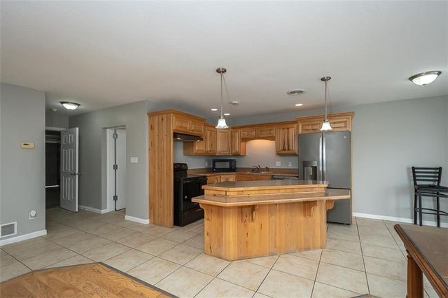 Kitchen featuring black appliances, light tile patterned floors, visible vents, and a kitchen island | Image 10