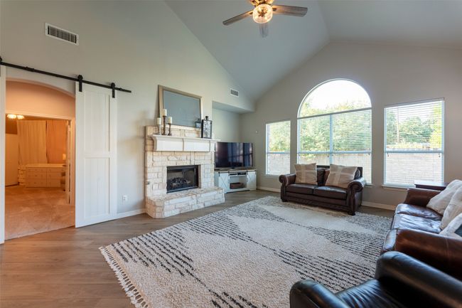 Living area with a barn door, ceiling fan, wood finished floors, high vaulted ceiling, and a fireplace | Image 10