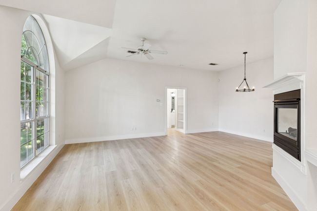 Unfurnished living room with healthy amount of natural light, light wood-type flooring, a ceiling fan, a multi sided fireplace, and vaulted ceiling | Image 7