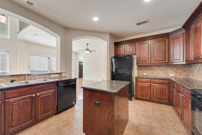 Kitchen featuring black appliances, arched walkways, a kitchen island, backsplash, and light tile patterned floors | Image 7
