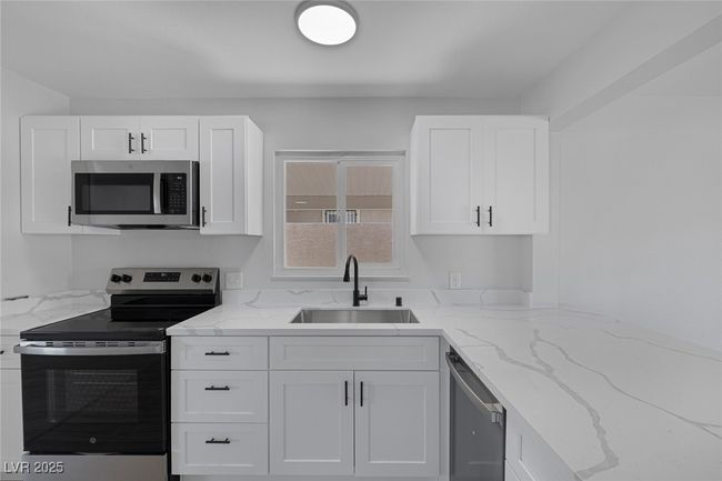 Kitchen with stainless steel appliances, white cabinets, and light stone countertops | Image 10
