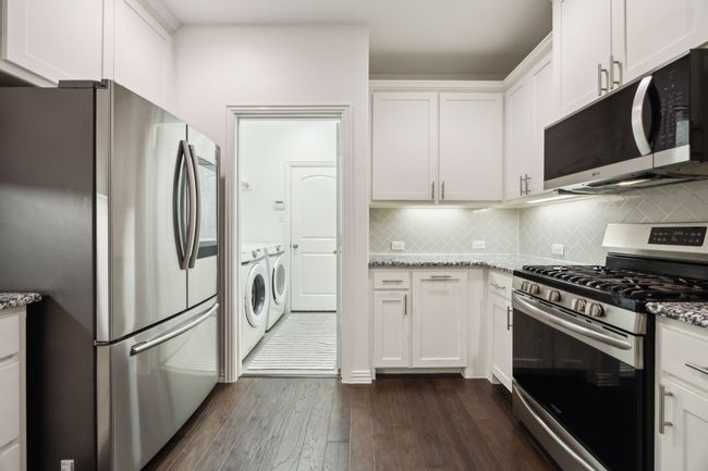 Kitchen featuring washing machine and clothes dryer, white cabinets, stainless steel appliances, dark wood-style flooring, and light stone countertops | Image 7