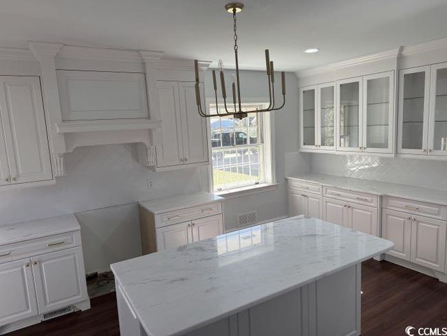 Kitchen featuring white cabinets, light stone counters, dark wood-type flooring, and decorative light fixtures | Image 5