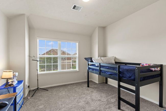 This is a cozy, carpeted bedroom with neutral walls, featuring a window that allows ample natural light. It includes a loft bed and a small desk area, perfect for a child's room or a compact office space. | Image 27