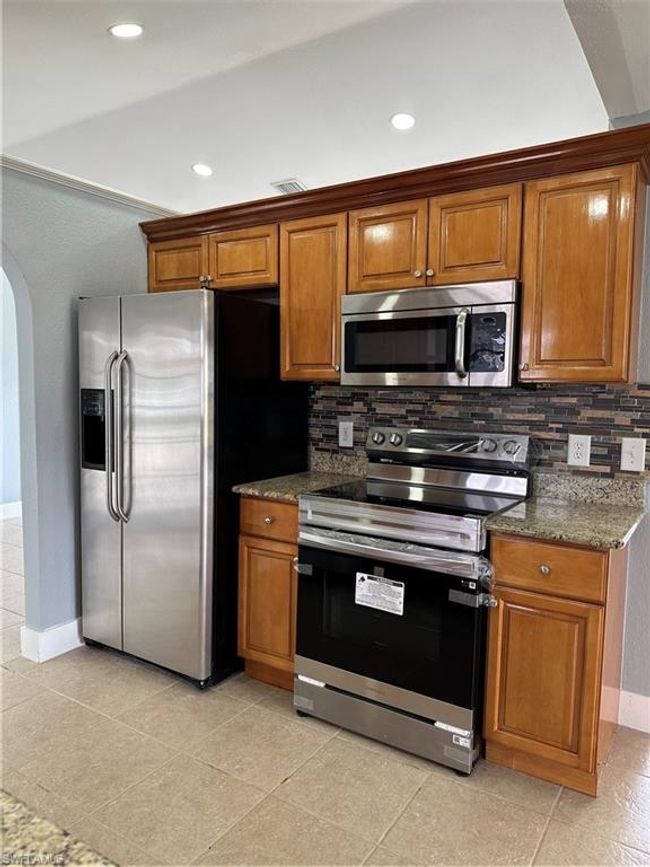 Kitchen with stove, refrigerator, arched walkways, backsplash, and brown cabinetry | Image 12