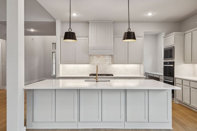 Kitchen featuring stainless steel appliances, tasteful backsplash, light countertops, light wood-style floors, and an island with sink | Image 9