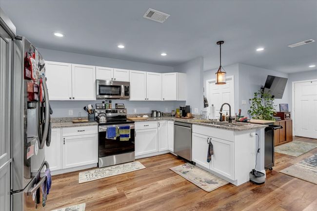 Kitchen featuring appliances with stainless steel finishes, a peninsula, white cabinets, recessed lighting, and light stone counters | Image 8