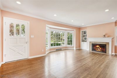 Unfurnished living room with a tile fireplace, built in shelves, ornamental molding, and light hardwood / wood-style flooring | Image 3