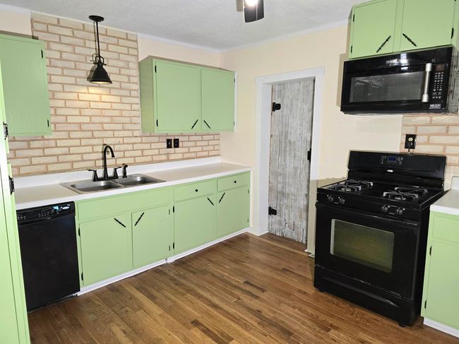 Kitchen featuring dark wood-type flooring, green cabinetry, pendant lighting, black appliances, and sink | Image 8