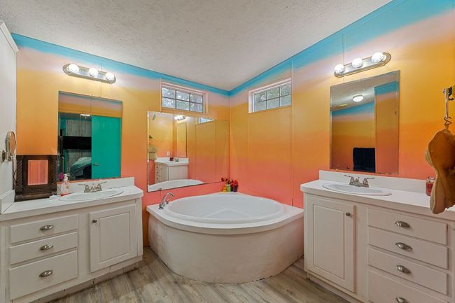 Bathroom featuring a textured ceiling, wood finished floors, lofted ceiling, two vanities, and a garden tub | Image 6