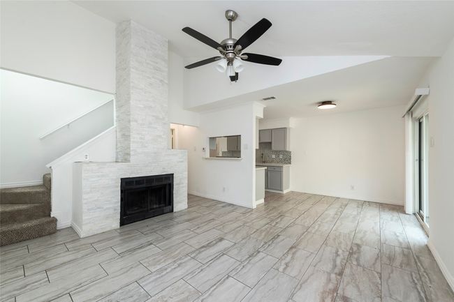 Unfurnished living room with a fireplace, a ceiling fan, stairs, visible vents, and high vaulted ceiling | Image 5