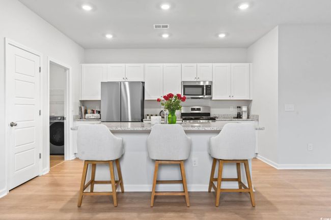 Kitchen featuring appliances with stainless steel finishes, washer / dryer, a kitchen bar, light wood-style flooring, and recessed lighting | Image 4