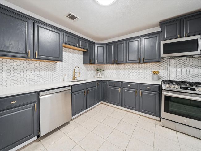 Kitchen with appliances with stainless steel finishes, a sink, light countertops, light tile patterned flooring, and backsplash | Image 8