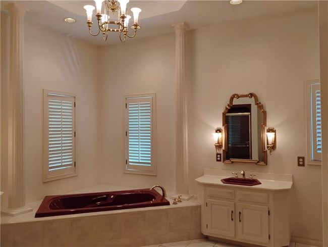 Full bath with a jetted bath, an inviting chandelier, vanity, and decorative columns | Image 49