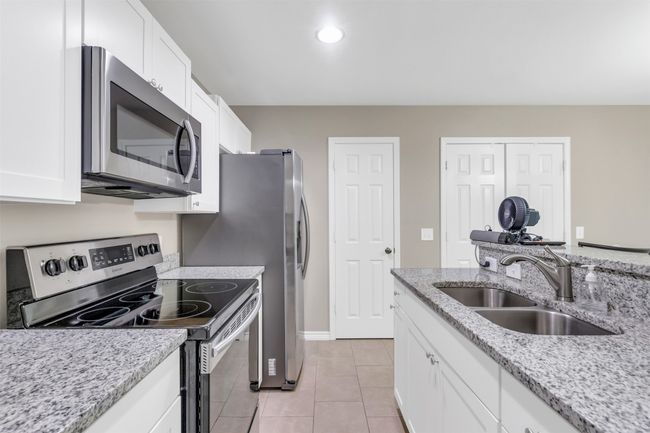 Kitchen with stainless steel appliances, white cabinetry, light tile patterned floors, light stone counters, and recessed lighting | Image 8