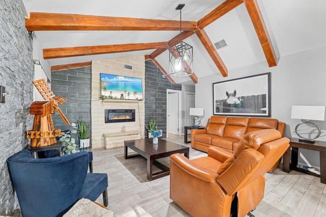Living room with light wood finished floors, beam ceiling, a glass covered fireplace, and visible vents | Image 11