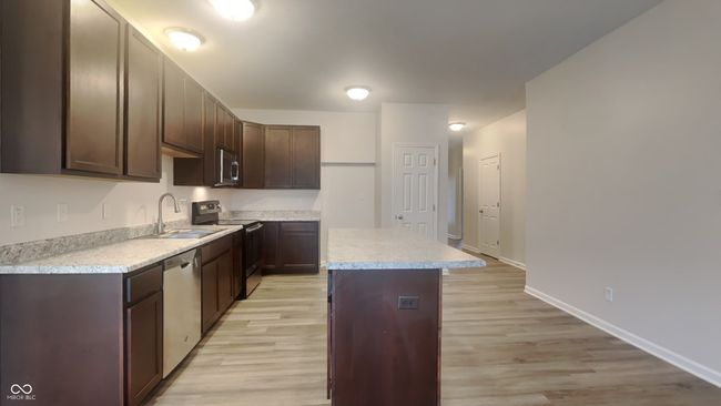 kitchen with a sink, stainless steel appliances, a center island, dark brown cabinetry, and light countertops | Image 6