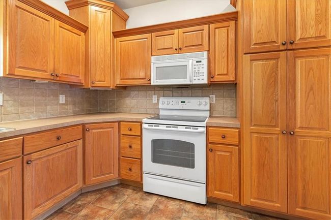 Kitchen with light countertops, decorative backsplash, white appliances, and stone finish flooring | Image 16