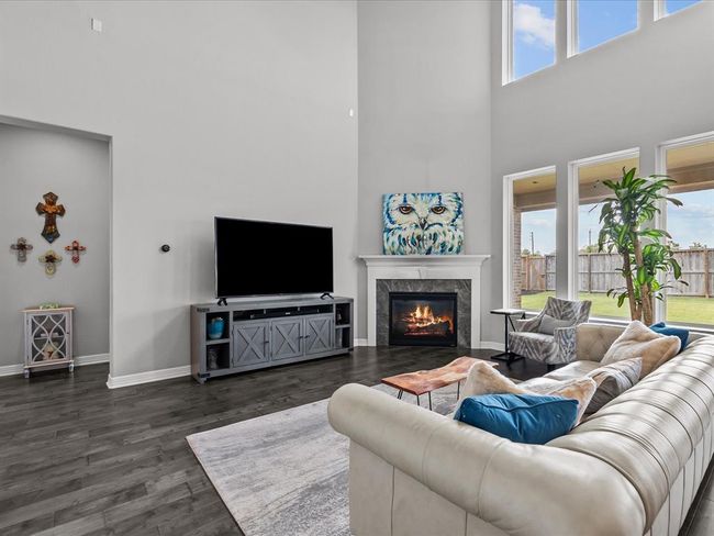 The living room open to the kitchen features wood flooring, two-story high ceilings, a wall of windows and a cozy fireplace for those cold winter nights | Image 4