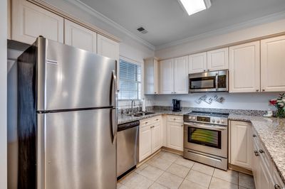 Kitchen featuring light tile patterned flooring, crown molding, sink, light stone counters, and appliances with stainless steel finishes | Image 3