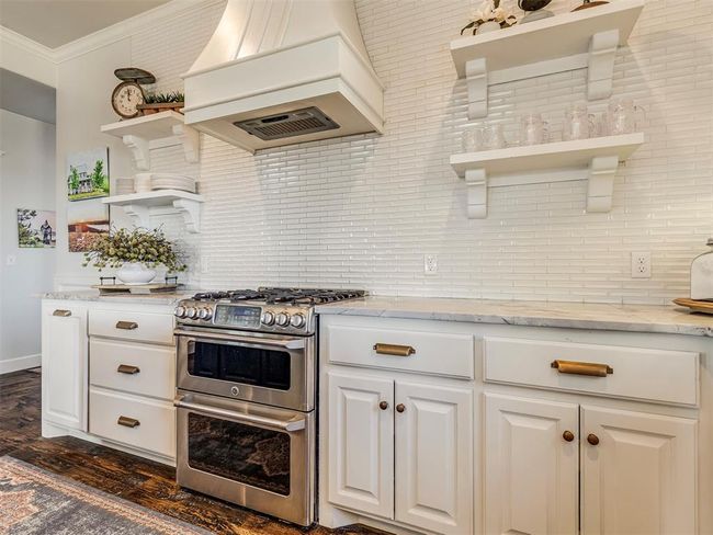 Kitchen with range with two ovens, decorative backsplash, custom exhaust hood, crown molding, and open shelves | Image 10