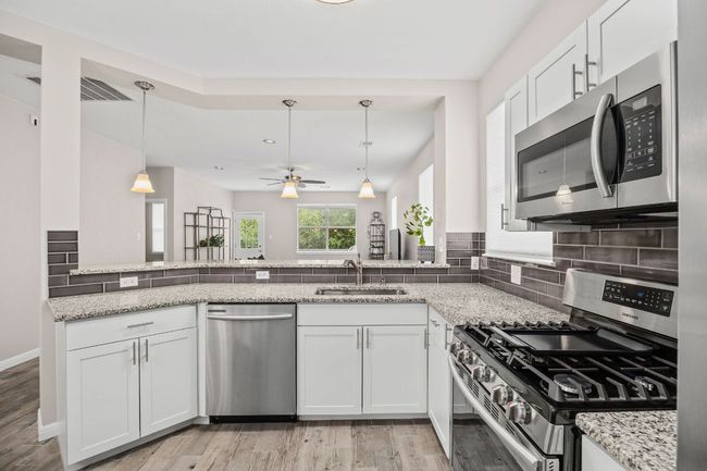 Kitchen with tasteful backsplash, light stone countertops, appliances with stainless steel finishes, light wood finished floors, and a sink | Image 17