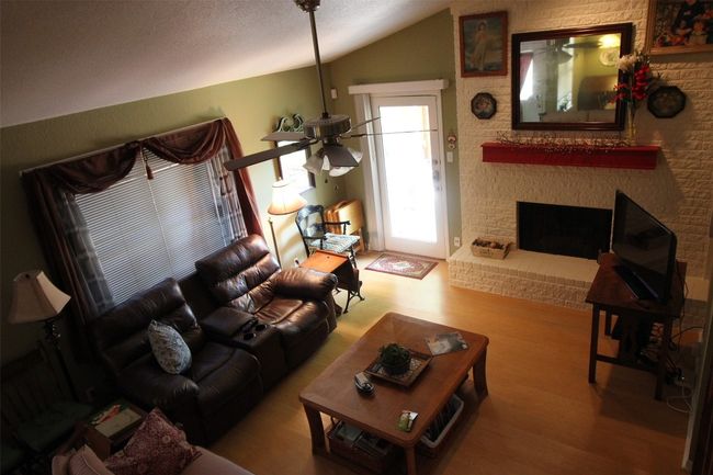 Living area with vaulted ceiling, wood finished floors, a brick fireplace, and a ceiling fan | Image 7
