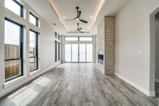 Unfurnished living room with ceiling fan, a raised ceiling, a healthy amount of sunlight, and light hardwood / wood-style floors | Image 5