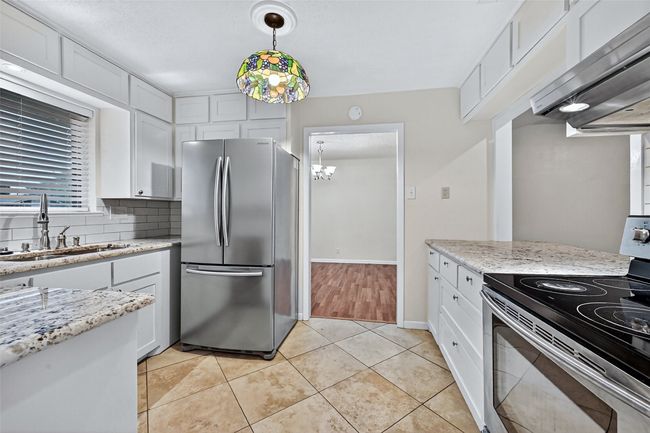 Kitchen featuring appliances with stainless steel finishes, extractor fan, white cabinetry, light stone countertops, and decorative light fixtures | Image 9