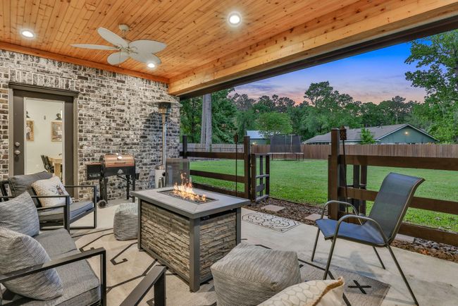 This cozy outdoor patio features a wooden ceiling with recessed lighting and a ceiling fan, a modern fire pit with comfortable seating, and a view of a spacious backyard. Ideal for relaxation and entertaining. | Image 6